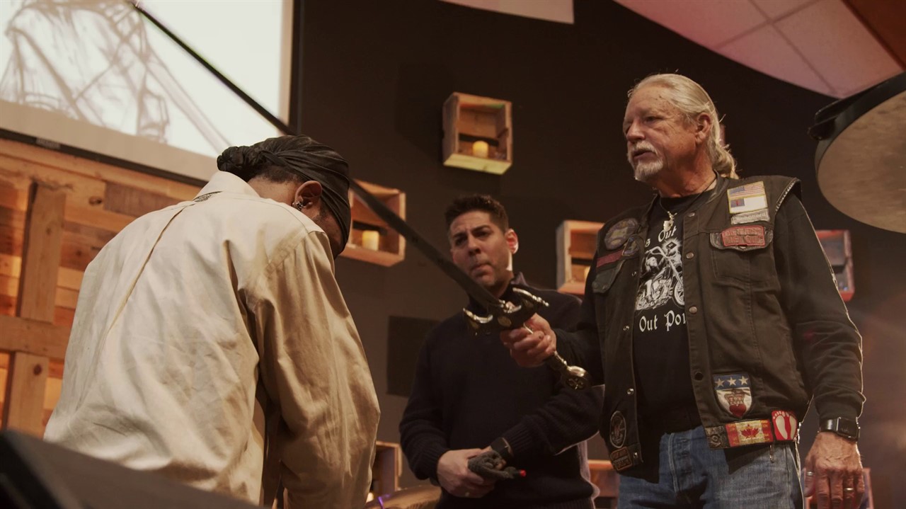A man is knighted by a man in a biker jacket