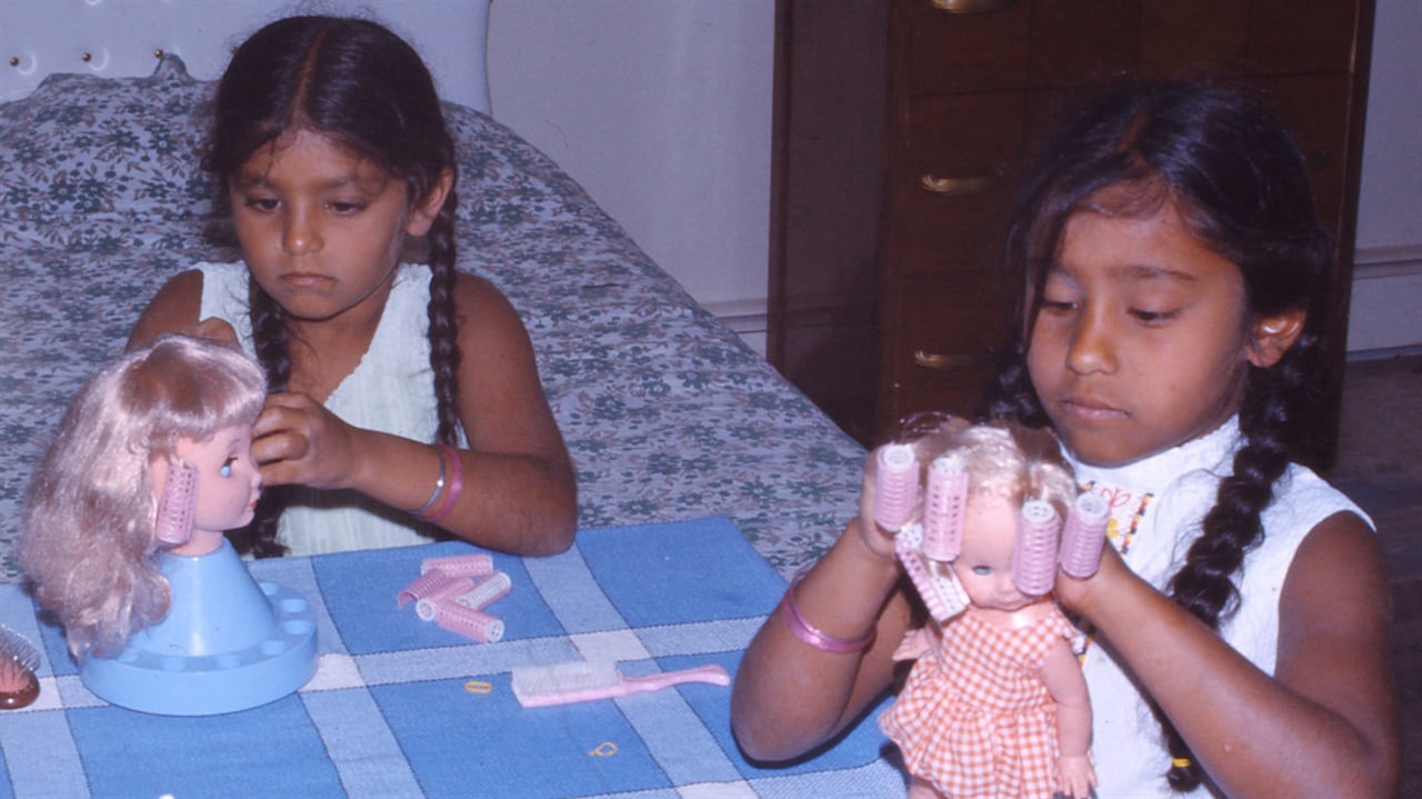 Two brown skined girls play with white dolls