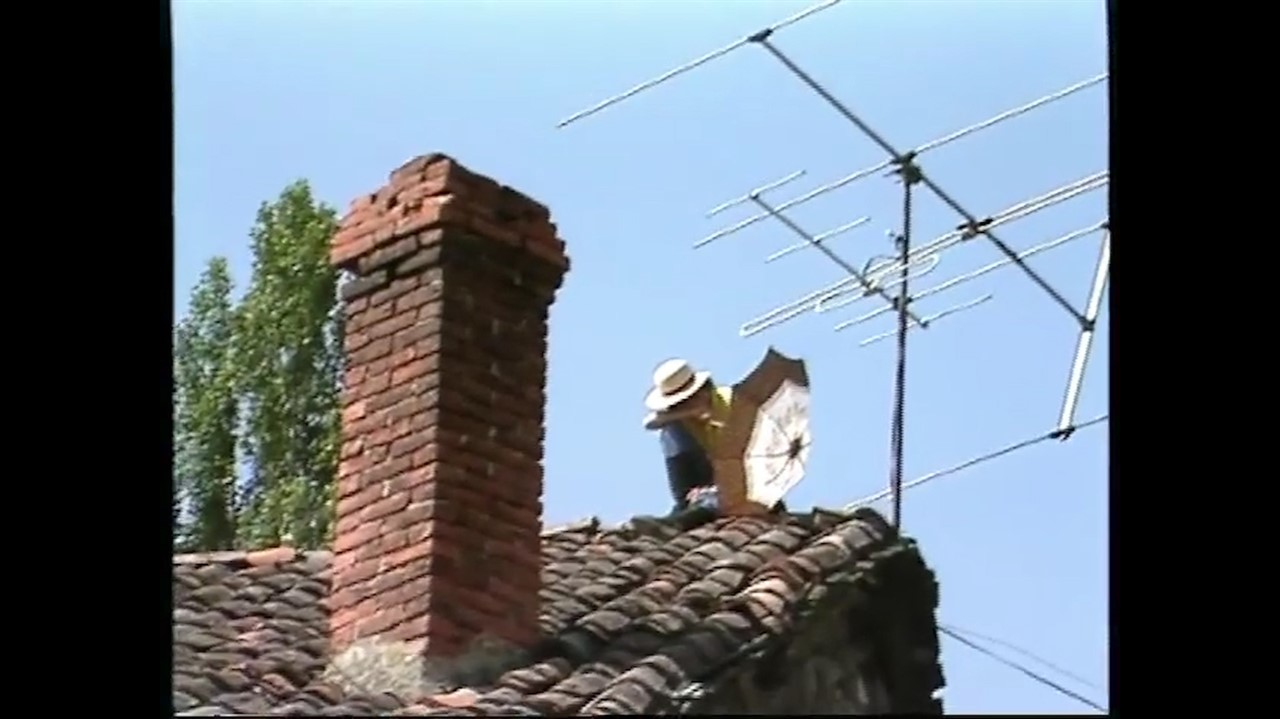 Person pearched on a roof beside a brick chimney