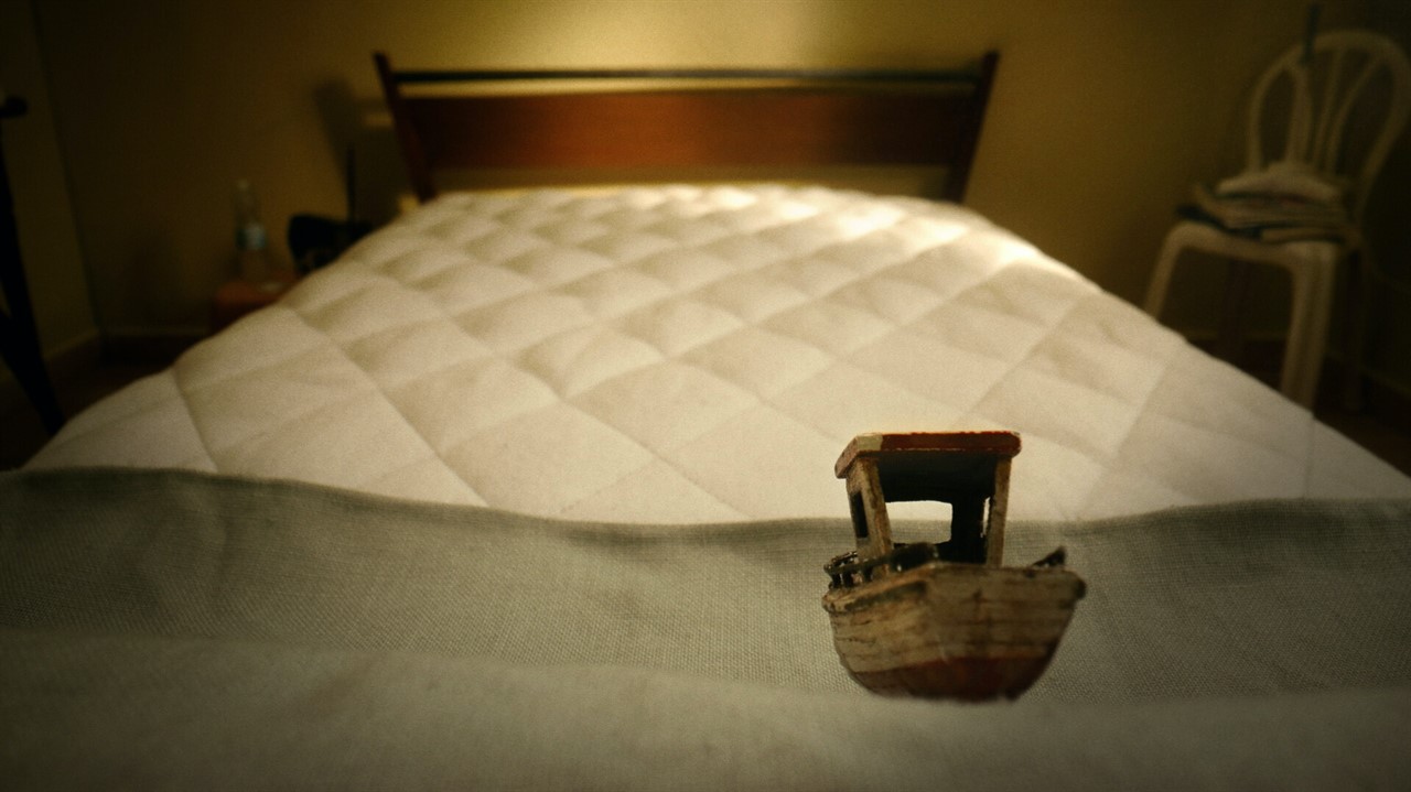 A small wooden boat sits on an unmade mattress