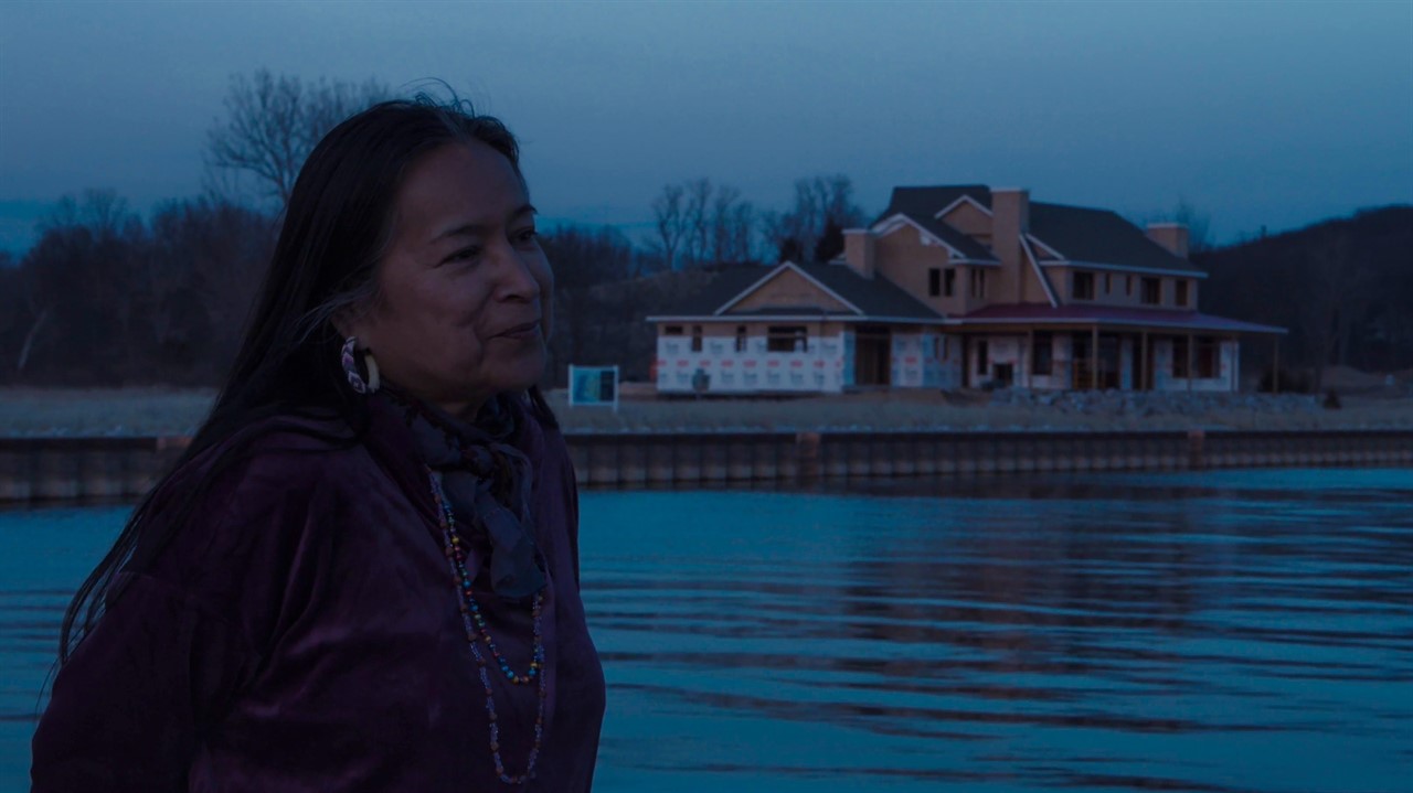 Woman beside a body of water. House behind