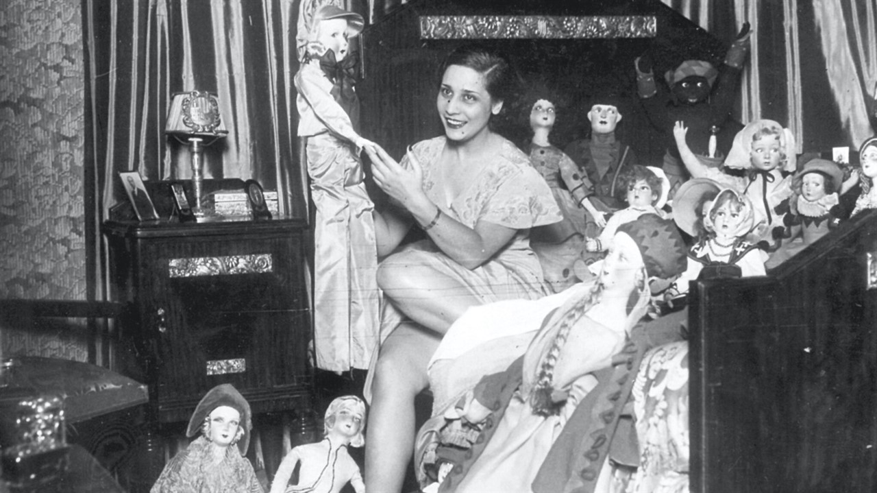 Woman sitting on a bed surrounded by dolls