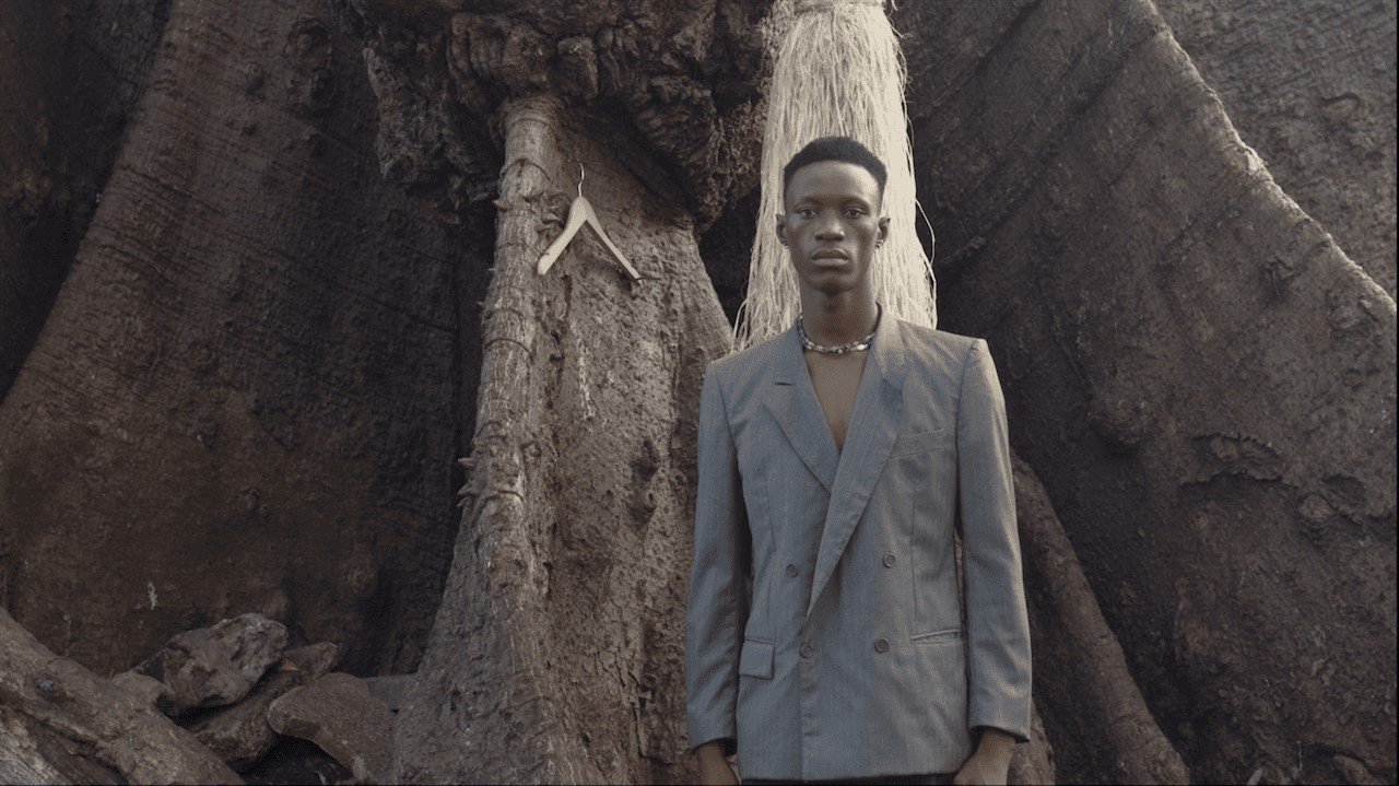 A young man in a suit stands in front of a giant t