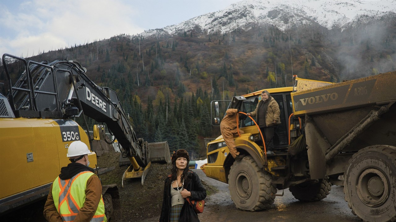 Woman stands beside large logging machines