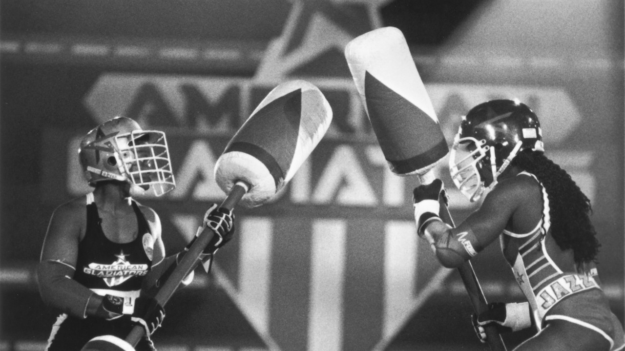 Two woman in protective gear holding padded clubs