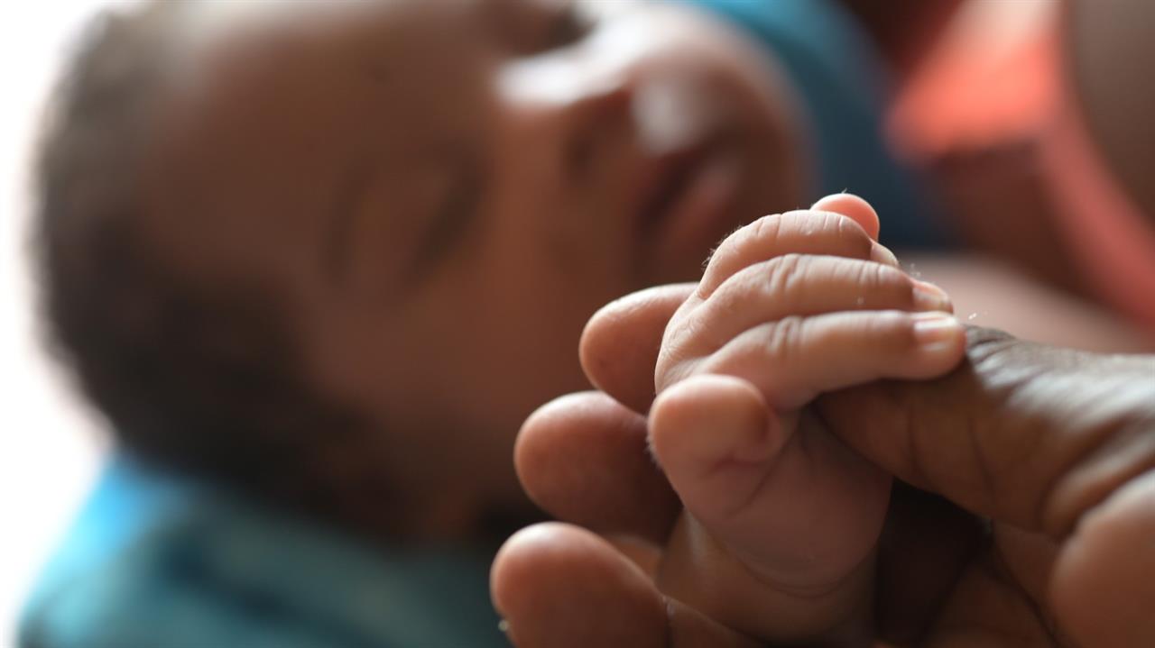 A newborns hand grabbing an adults thumb