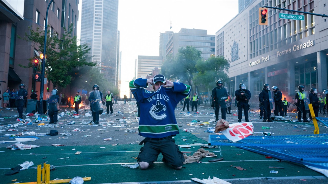 A man in a Canuks jersey kneels in the middle of p