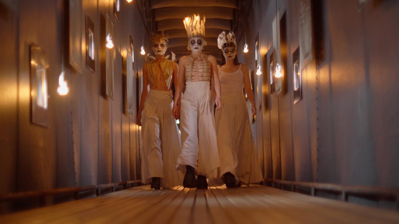 Three witches walk down a dimly lit hall