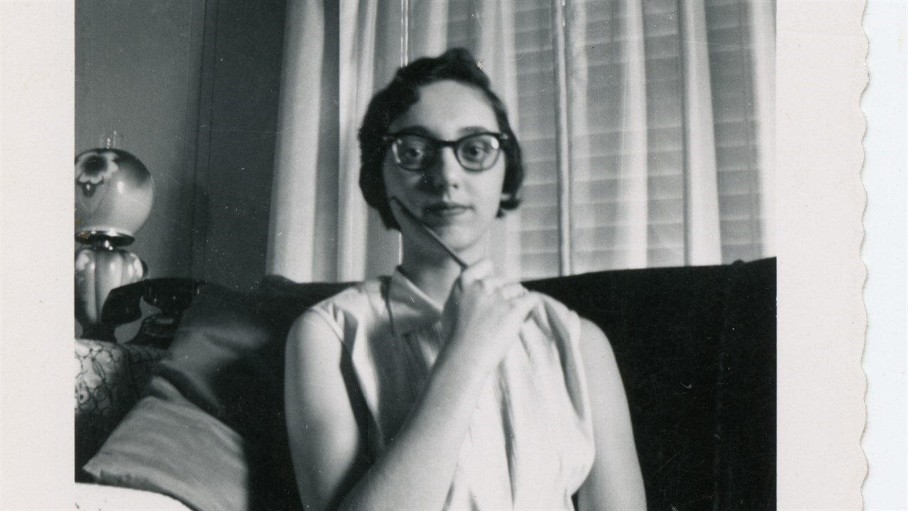 Joyce Carol Outes with glasses sitting on a couch