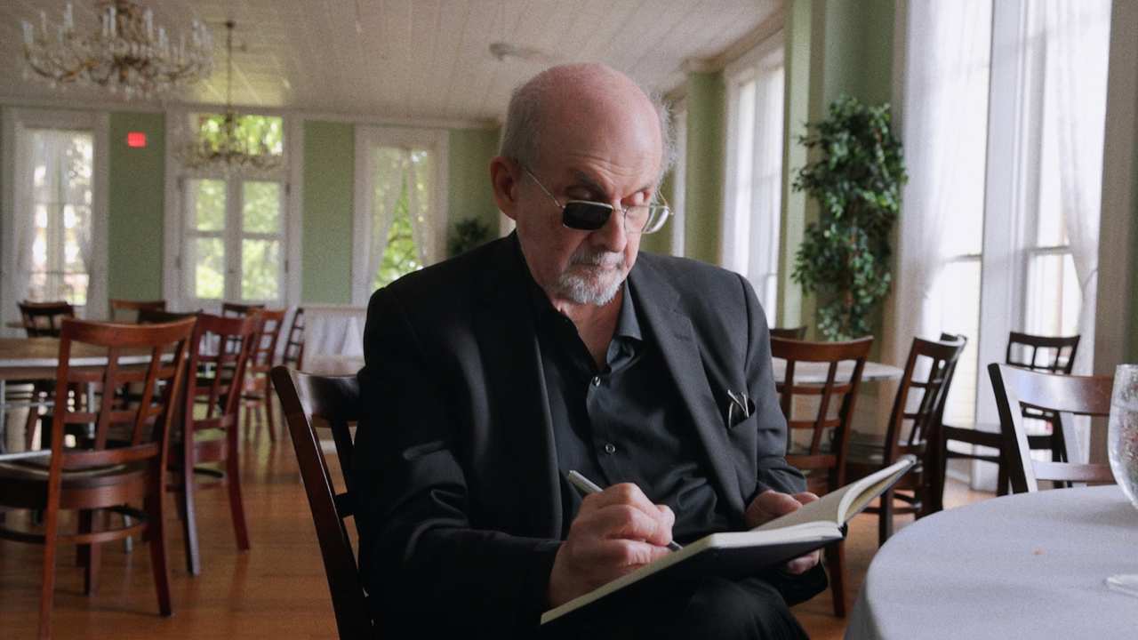 Salman Rushdie writing at a restaurant