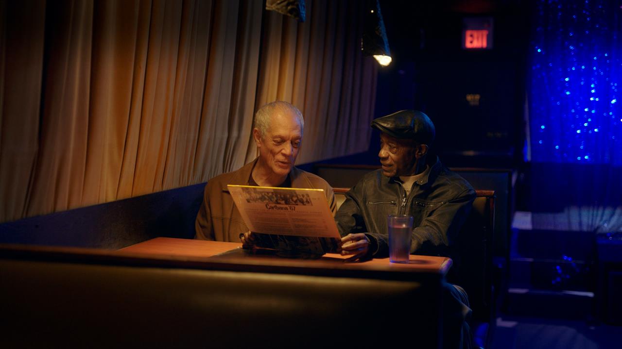 two men sitting in a booth looking at a record