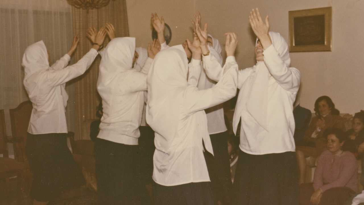 a group of women in white raising their hands