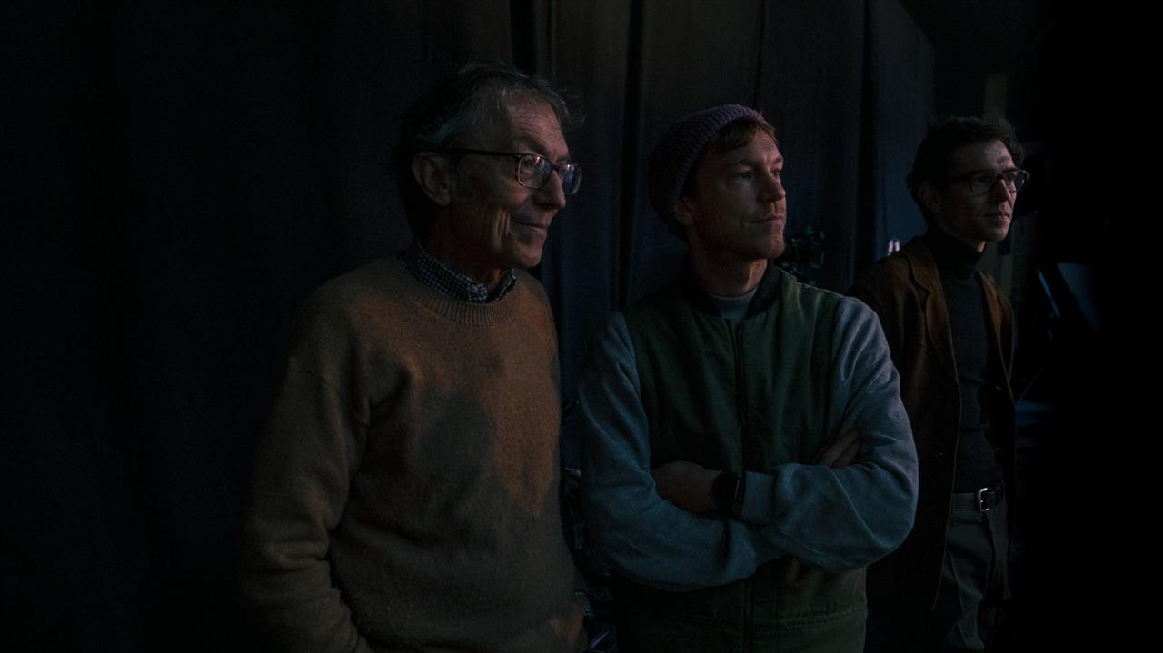 Three men standing in a dimly lit space