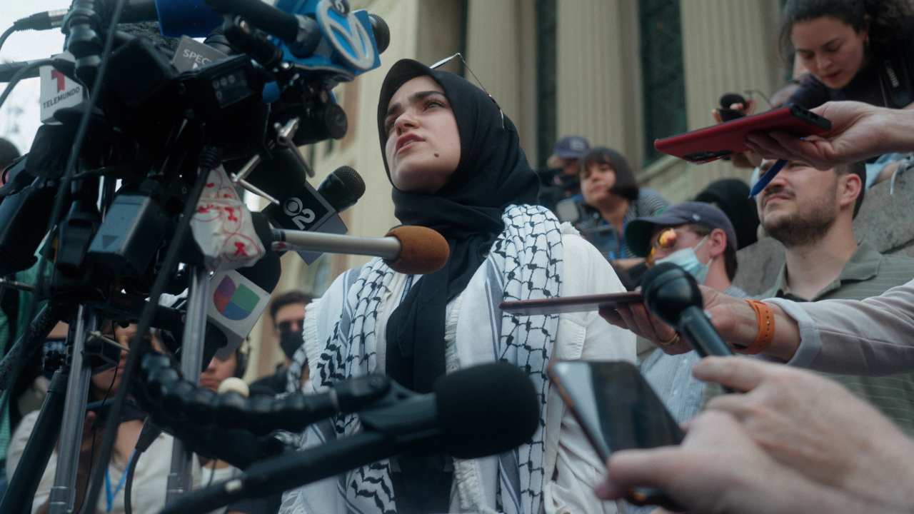a woman surrounded by reporters and microphone