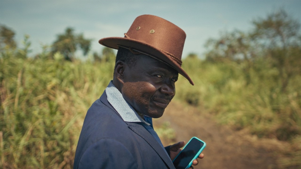 A man in a brimed hat, holding a cellphone, looks 