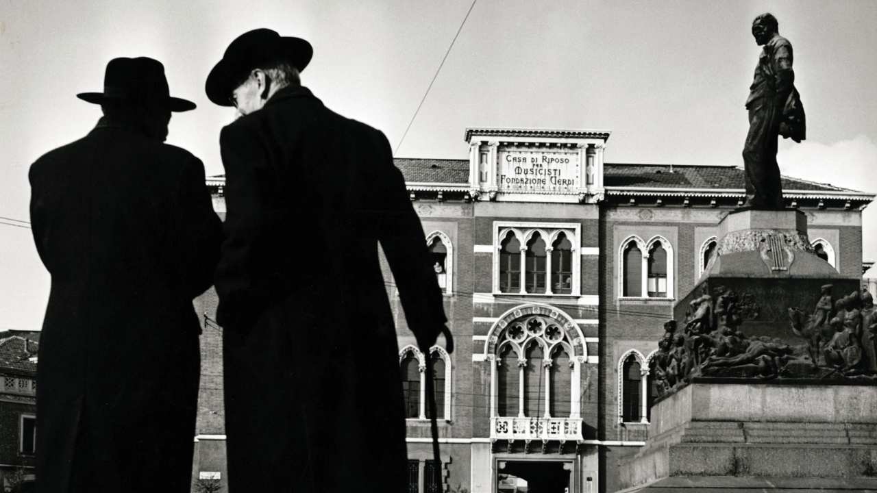 two men in black standing in front of a statue