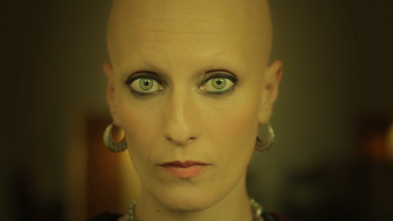 A bald woman with hoop earrings and eye makeup