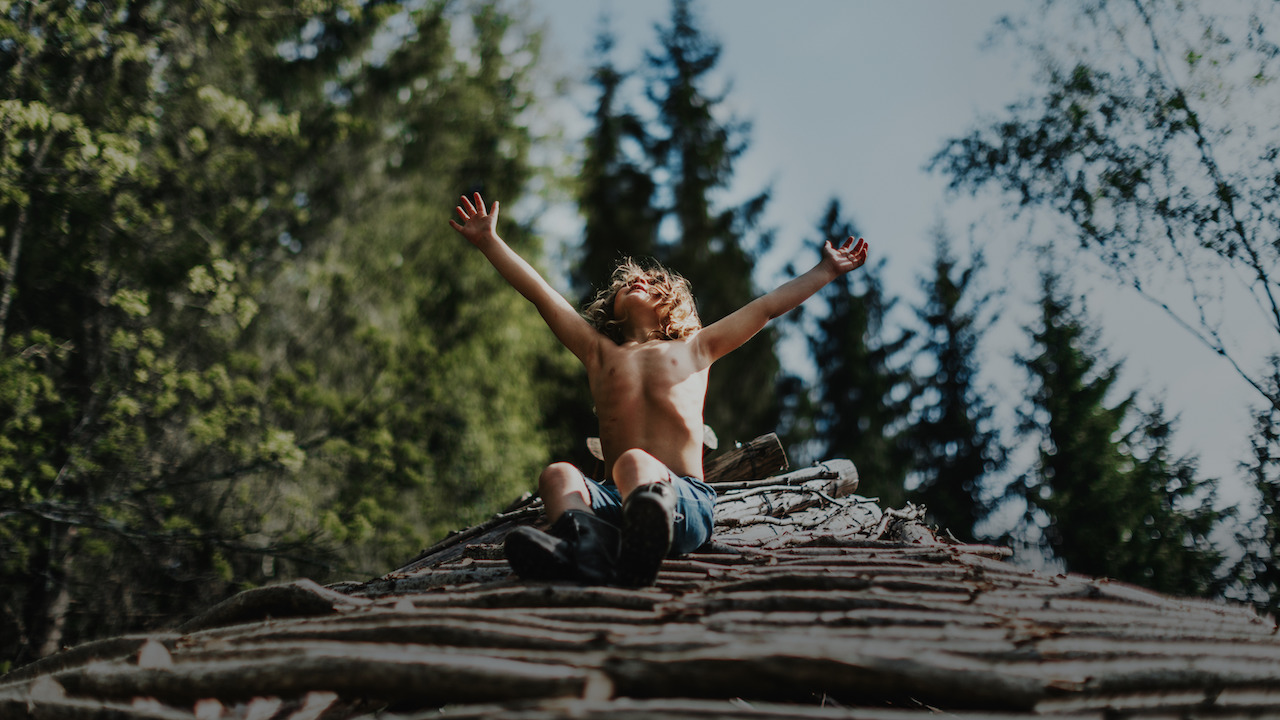 Child sits on a pile of logs, reaching to the sky