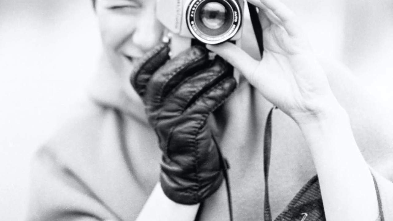 Woman wearing 1 leather glove, using a camera