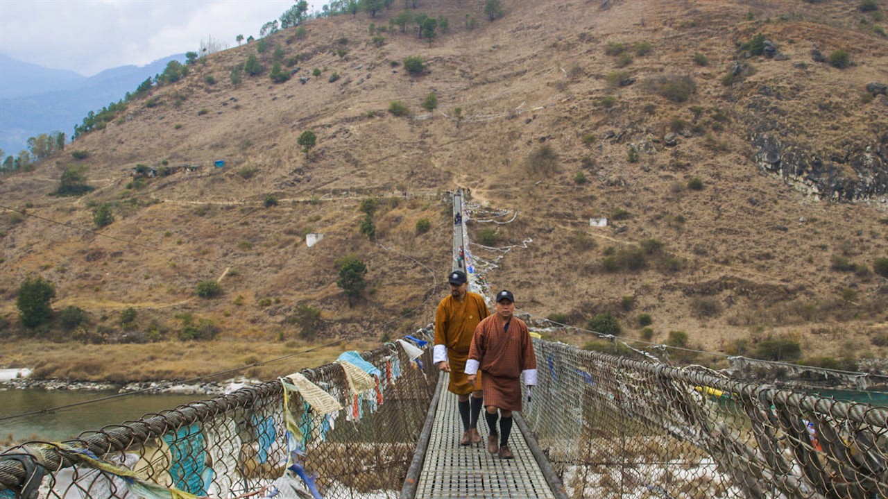 Two men walk across a chain-link bridge