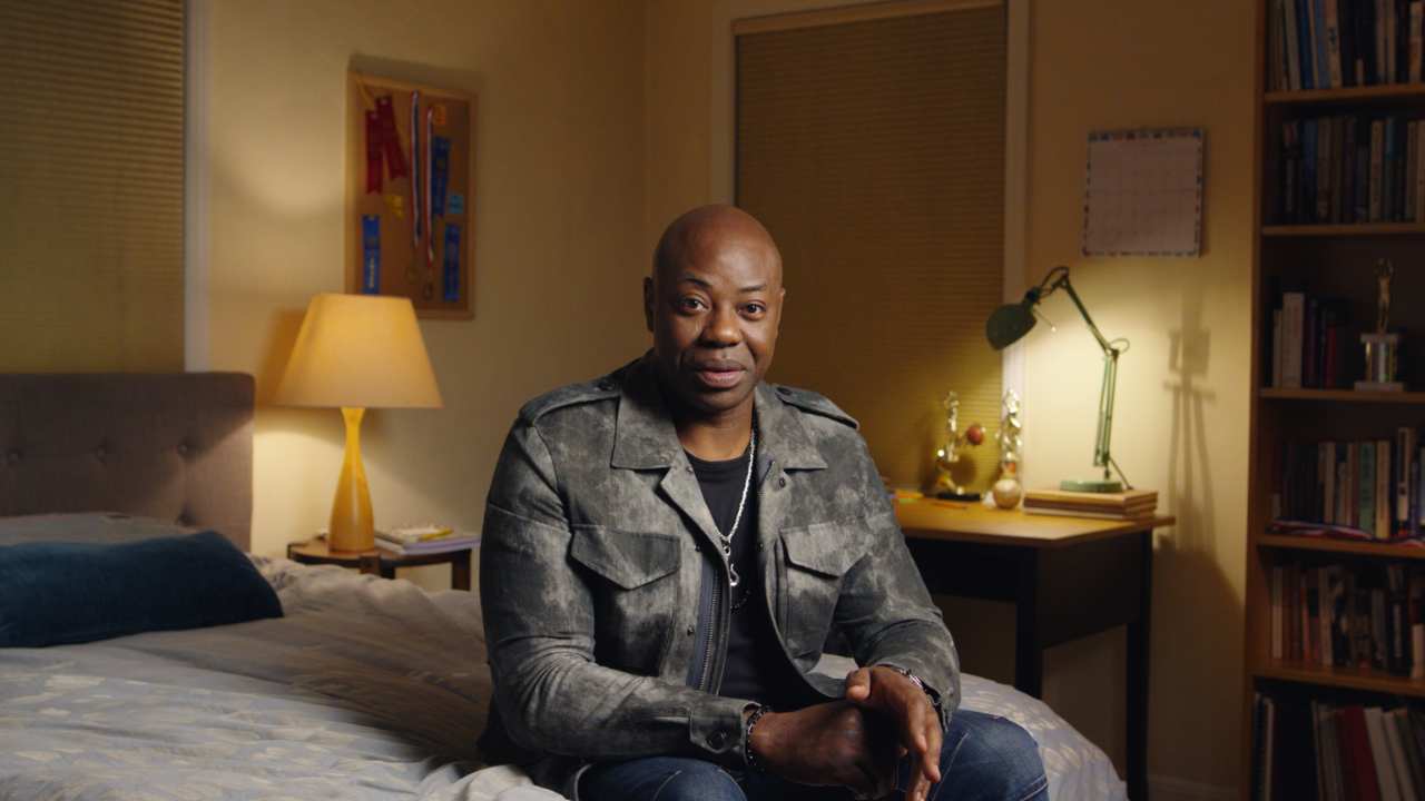 Dayo Ade sitting on a bed looking at the camera