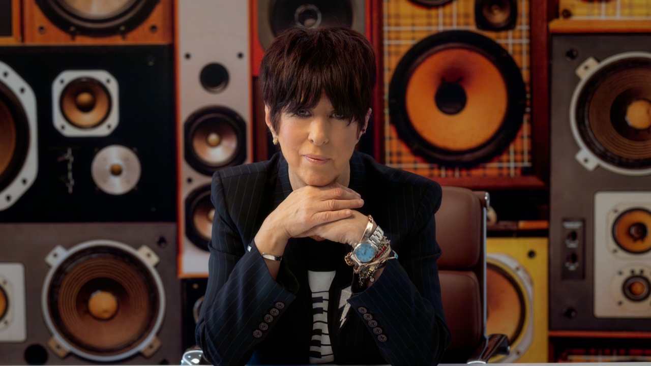 Diane Warren sitting at a desk in a blazer