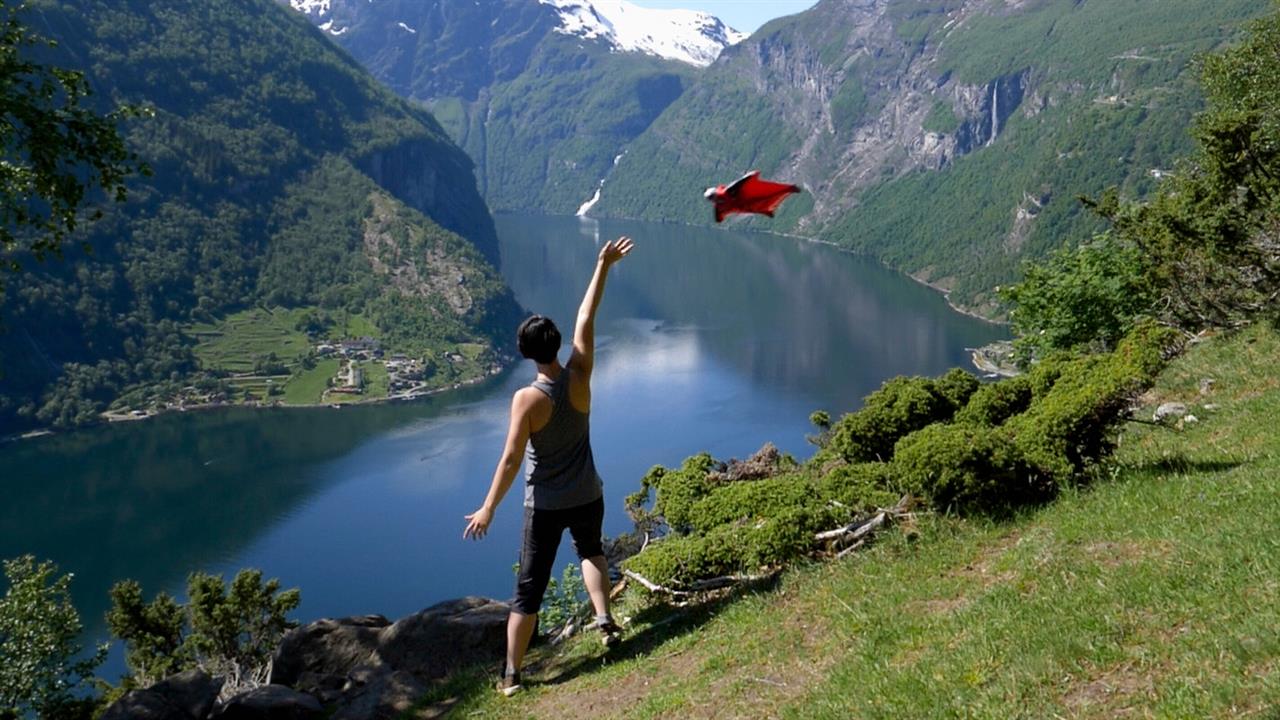 A person on a fjord waves to a flying person