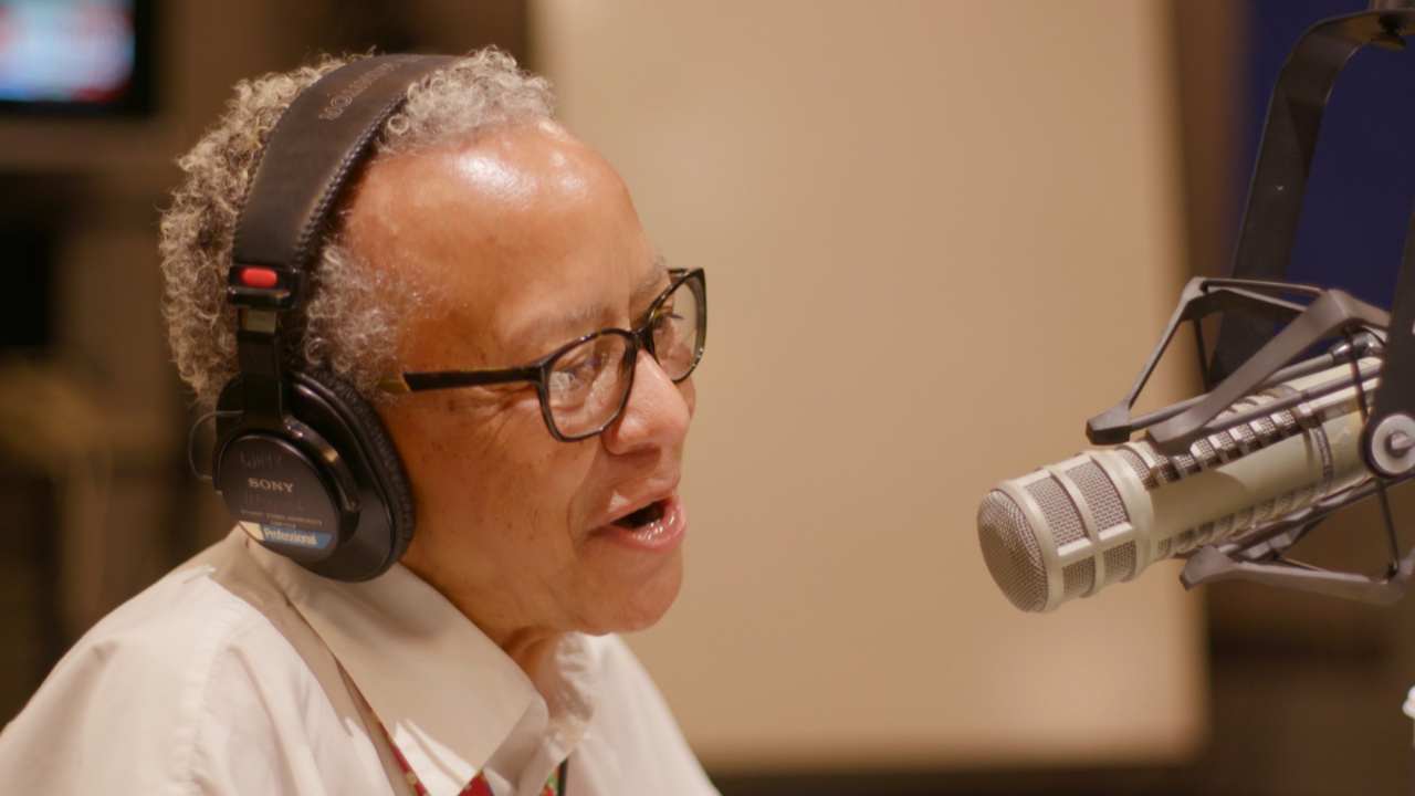 a woman with glasses and headphones speaking