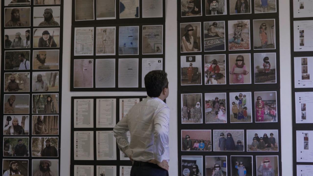 a man looking at a wall of photos and documents