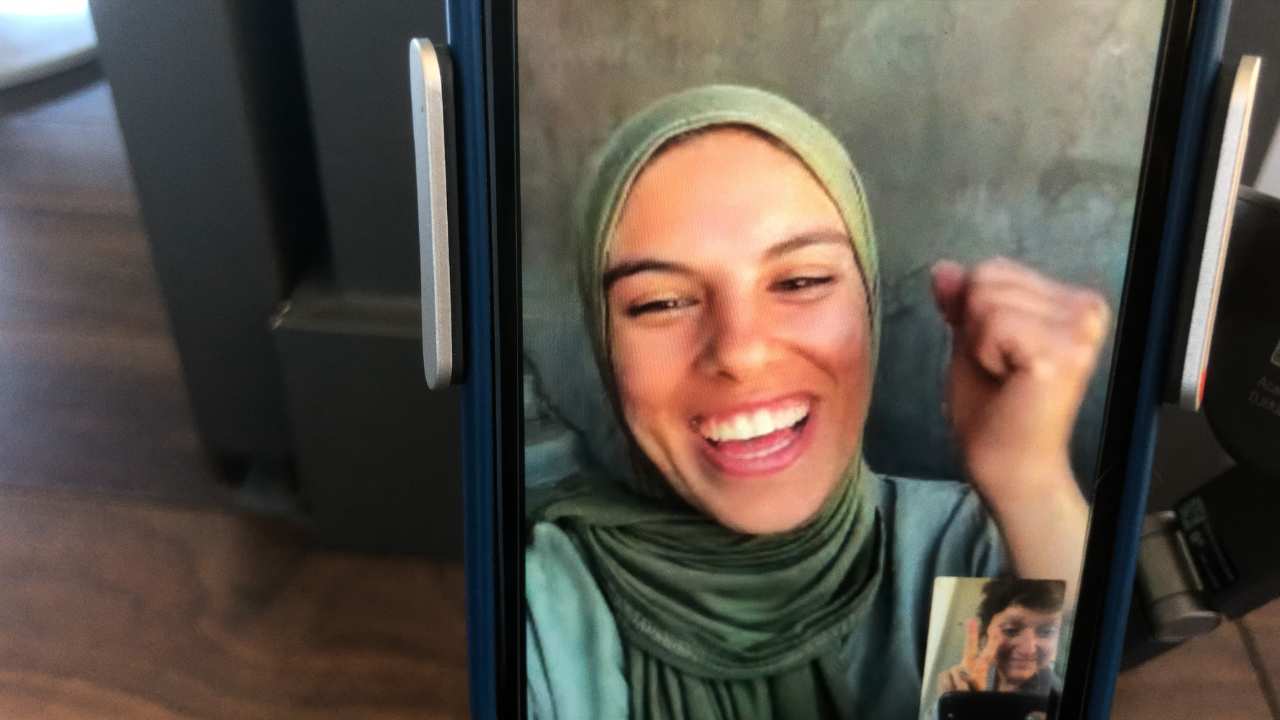 a woman in a head scarf smiling on a phone call