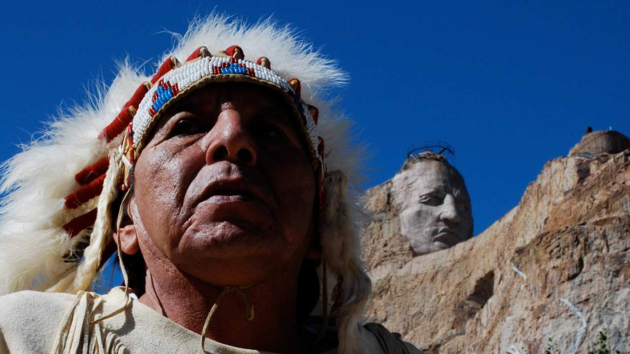 a man with a feathered headdress by Mount Rushmore