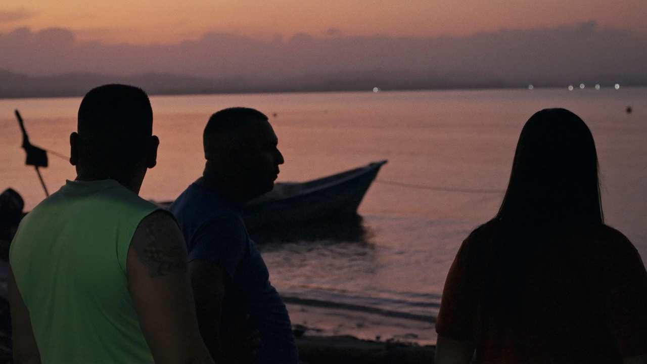 silhouette of three people by a boat at sunset
