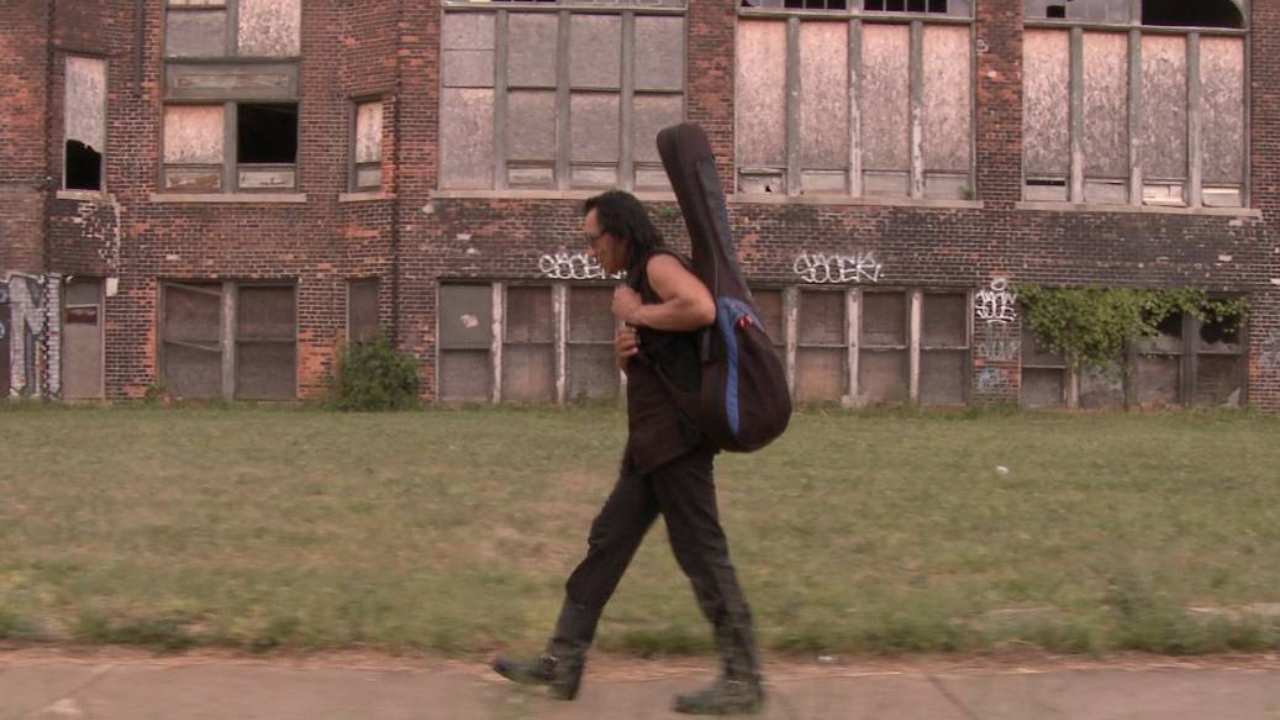 a man with sunglasses walking with a guitar