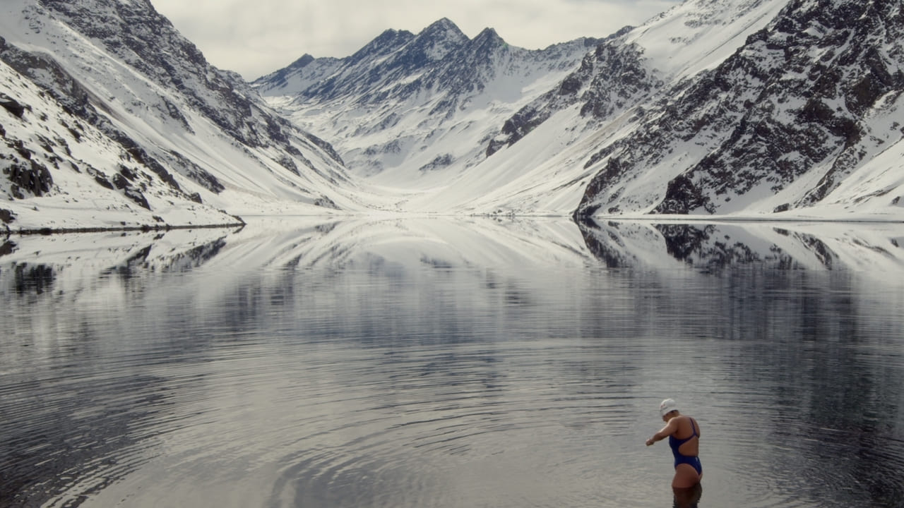 Woman stands in a lake surrounded by snowy mountai