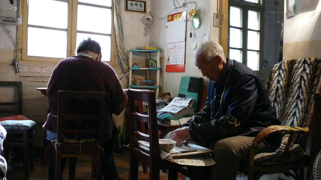 two elderly people sitting in a cluttered room