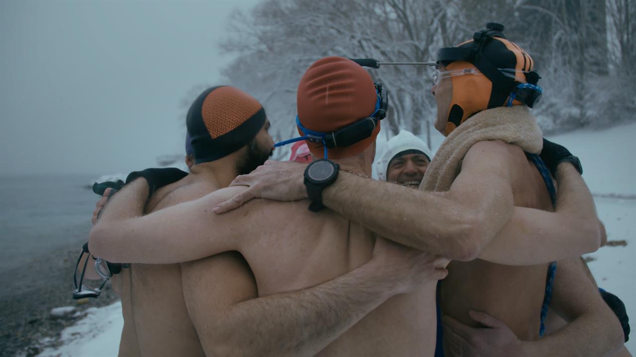 men hug in a circle before swimming in winter